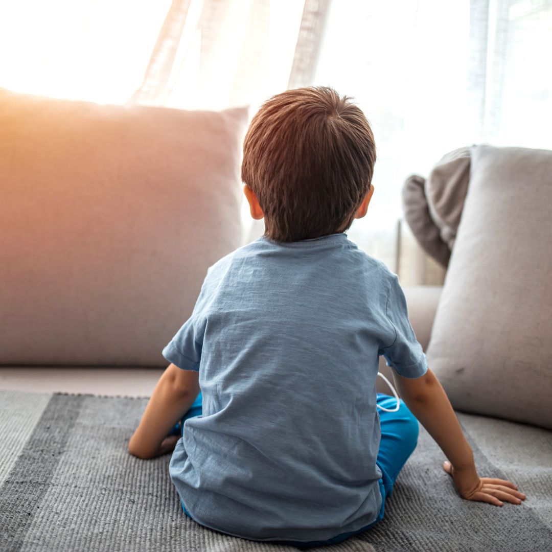 a child sitting alone on a couch looking out a window