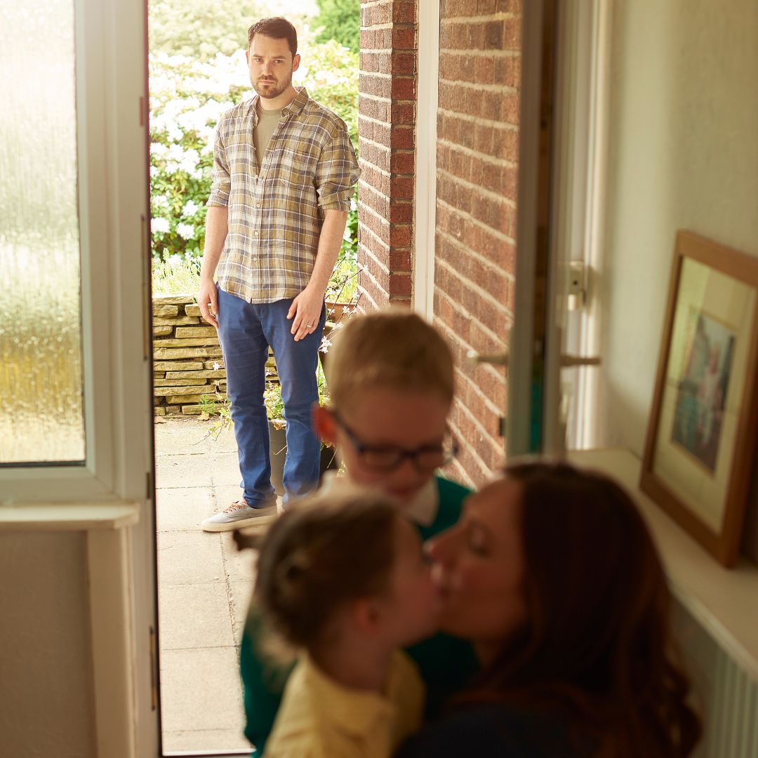 a person watching a mom hug her kids in an open front doorway