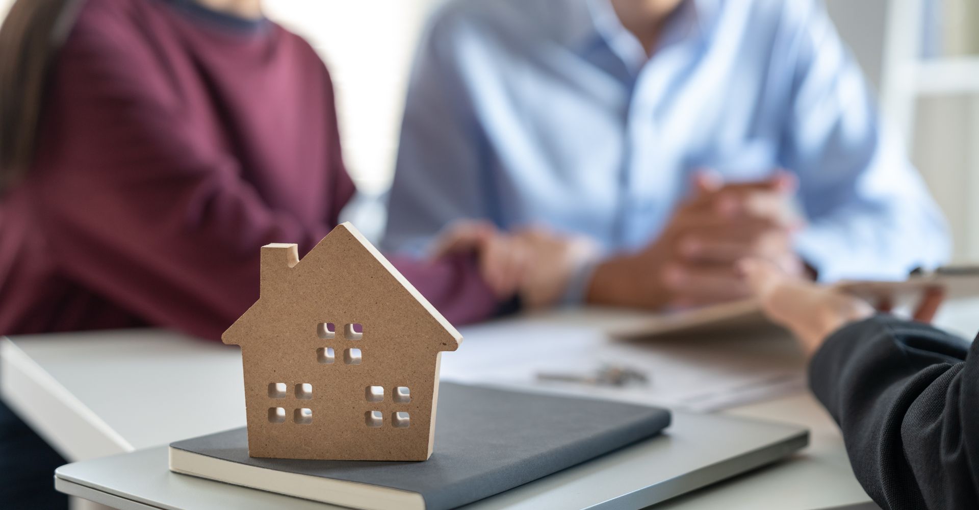 couple talking to lawyer with a wooden house toy in the foreground