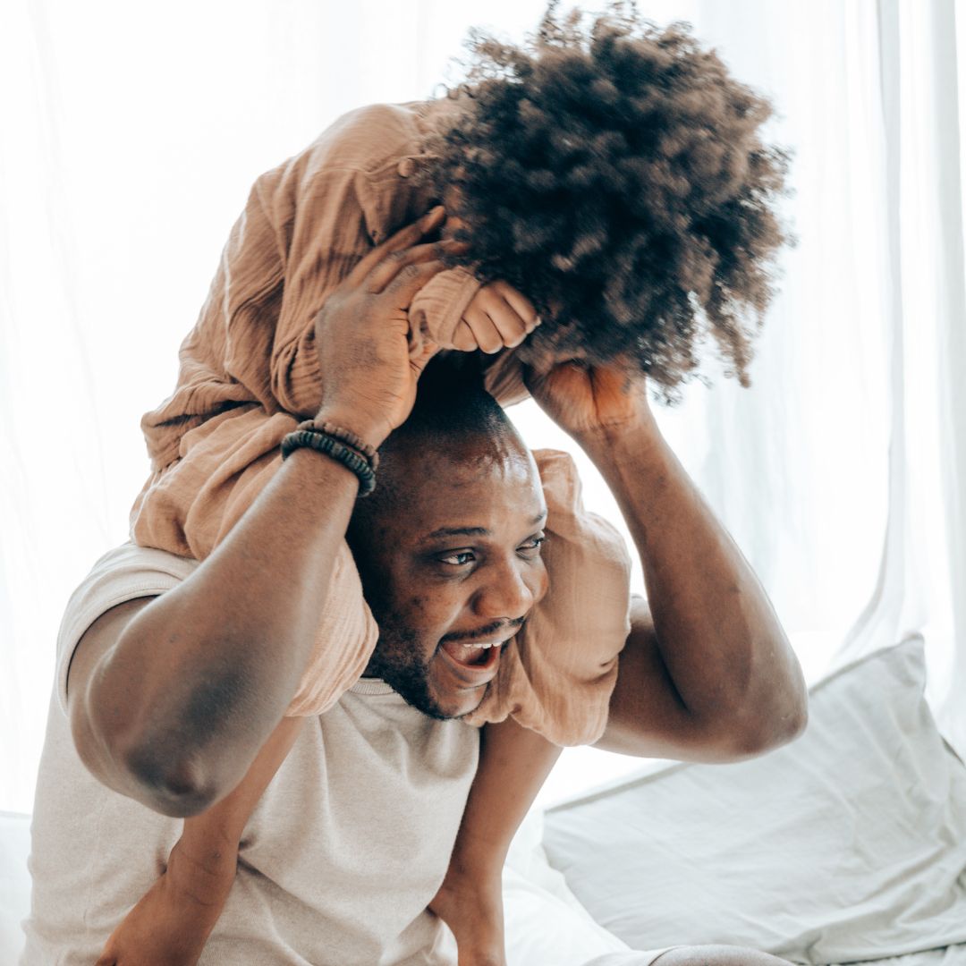 man has kid sitting on his shoulders and is laughing