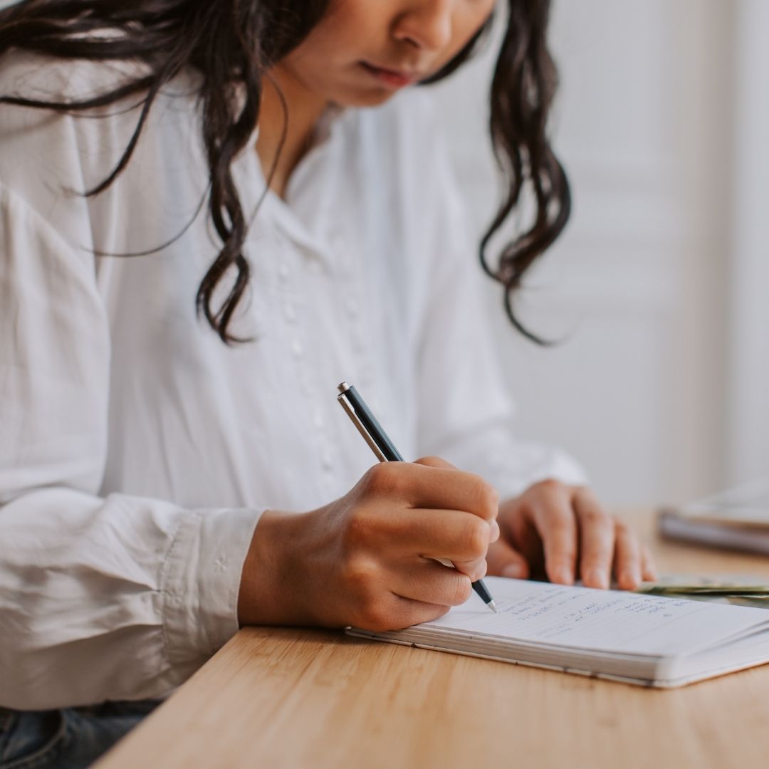 woman wearing blouse writes in journal 