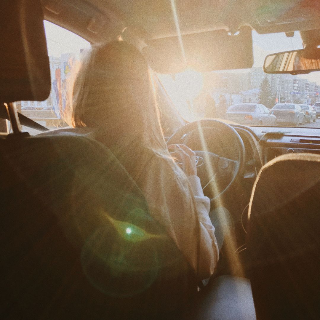 woman in drivers seat with sun coming through car windshield